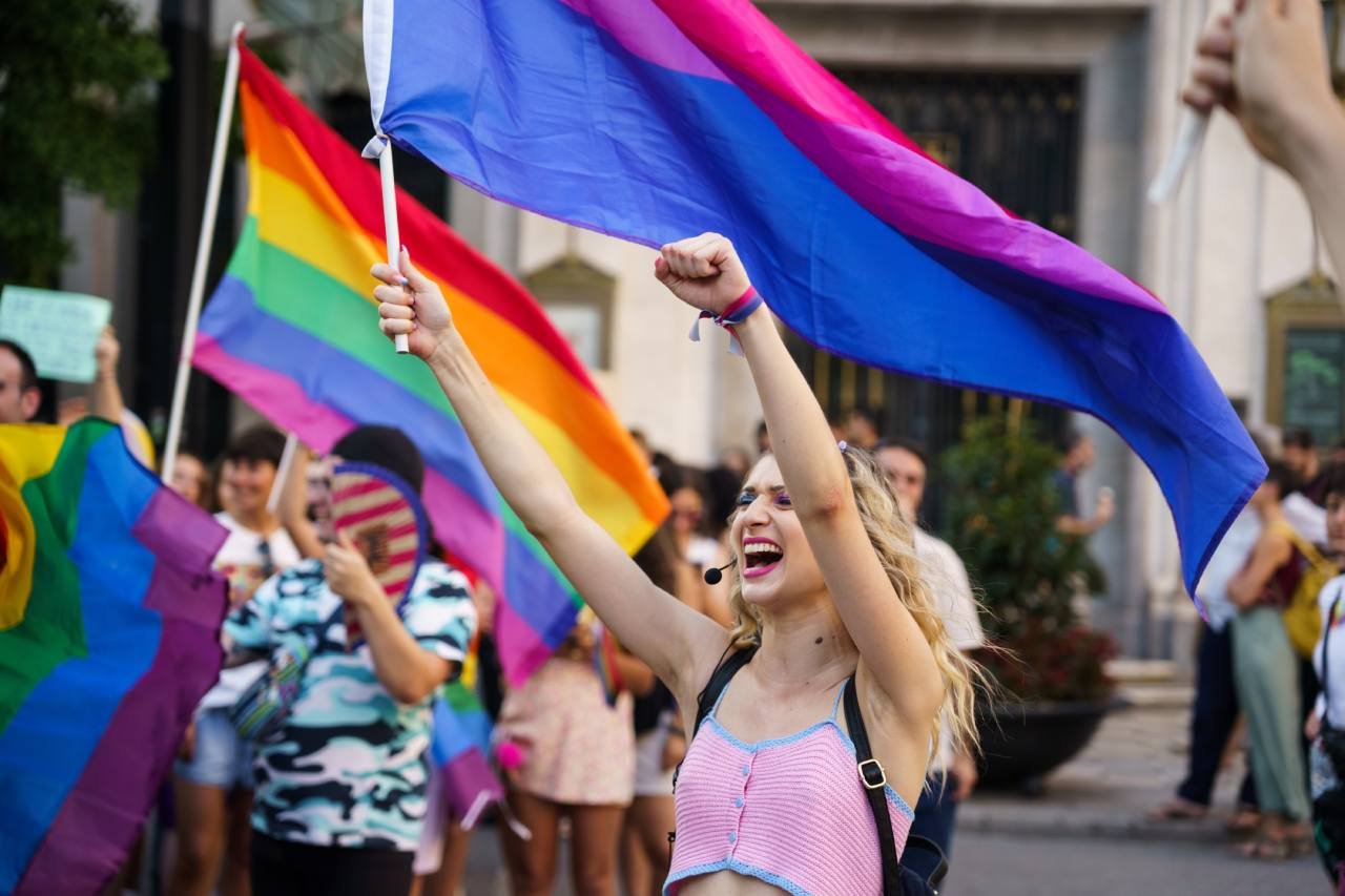 Blond person holding a trans flag and raising their fist in a parade - Granada Spain June 2023
